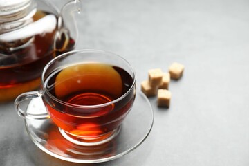 Aromatic black tea and brown sugar cubes on light grey table, closeup. Space for text