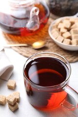 Aromatic black tea and brown sugar cubes on white table, closeup