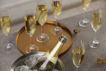 Bottle of sparkling wine in cooler bucket and glasses on grey table, closeup