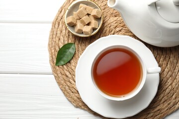 Aromatic black tea and brown sugar cubes on white wooden table, top view. Space for text