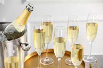 Bottle of sparkling wine in cooler bucket and glasses on table, closeup