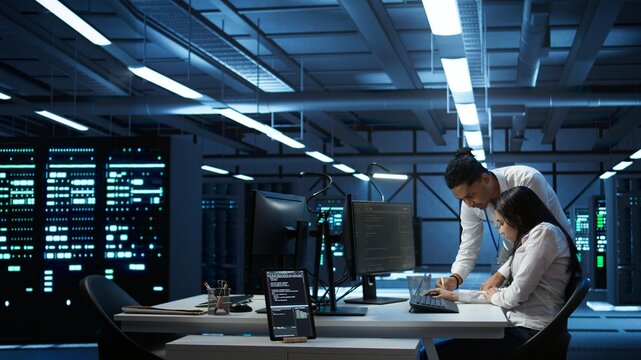 Teamworking colleagues in high tech data center managing and maintaining databases, ensuring data integrity, security and availability. Team of specialists updating server room systems, camera B - Powered by Adobe