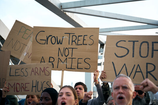 Anti-war placards at global protest by diverse large group of activists demonstrating together holding high cardboard banners for peace, love and no armies standing shouting peaceful slogans on bridge