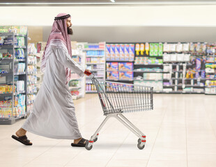 Full length profile shot of a saudi arab man walking and pushing a shopping cart