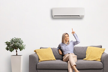 Woman sitting on a sofa and pointing at an air conditioning unit