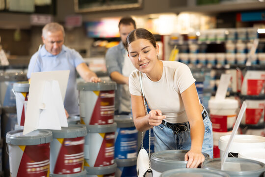Woman buys tin with paint in paintwork material department of construction store for carrying out internal finishing work on object