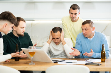 Fototapeta premium Men drink beer and try to help friend solve problems using laptop and the Internet