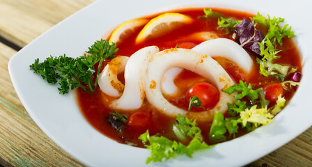 Bowl with dish of Mediterranean cuisine - tomato soup with squid and greens