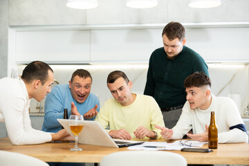 Fototapeta premium Group of men huddling around laptop at kitchen table, discussing problems and comforting distressed friend while gathering at home bachelor party