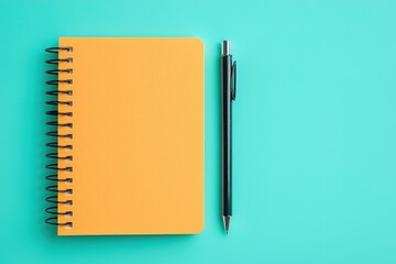 A bright orange notebook and a black pen are placed on a vibrant turquoise background, creating a visually appealing and minimalist workspace.