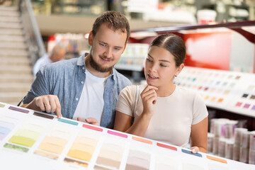 In store of building materials and repair materials, couple examines palette, chooses color of...