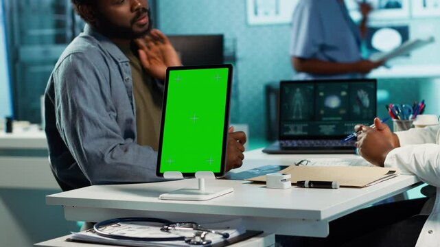 Black medic meets with patient next to isolated mockup display at the office, doing routine consultation and reviewing records for a treatment plan. Physician at private clinic. Camera A.