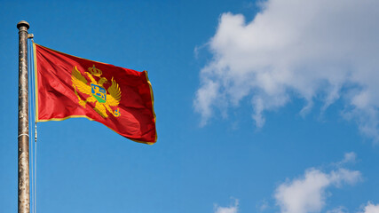 national flag of Montenegro waving against blue sky, official flag of the nation, blowing in the wind
