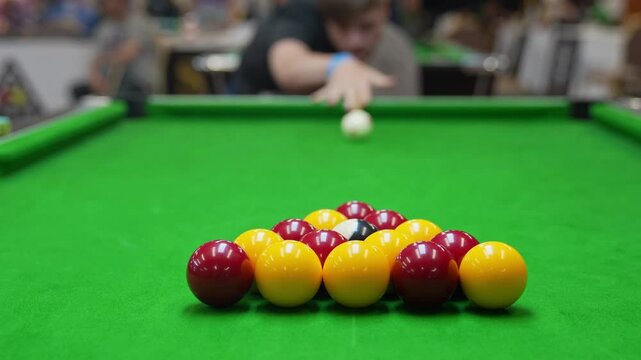 The break of red and yellow blackball Pool balls in a triangle on a green cloth pool table, hit by the cue with blur in the background 