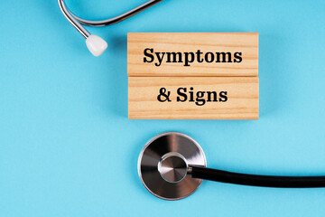 Stethoscope and wooden blocks with text Symptoms and Signs on blue background