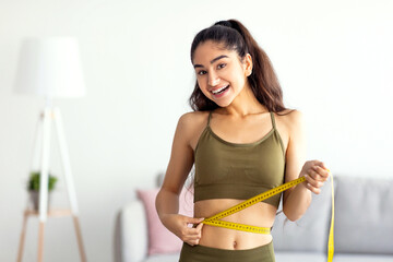 Successful weight loss concept. Slim Indian woman in sportswear measuring waist with tape,...