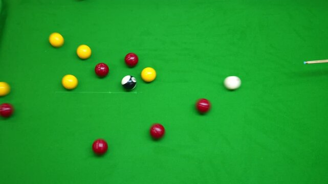 the break of red and yellow blackball Pool balls in a triangle on a green cloth pool table, hit by the cue from above