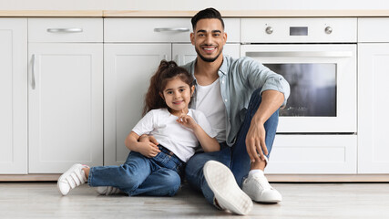 Happy middle eastern family father and daughter posing at kitchen, sitting on floor and hugging....