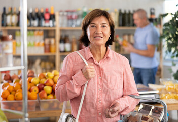 Elderly woman buyer with basket of food choosing products in grocery store