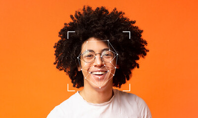 A person with curly hair and glasses smiles broadly, appearing cheerful. Their face is framed by a digital overlay indicating facial recognition technology against a vibrant orange backdrop.