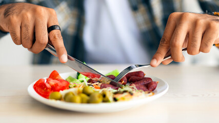Male hands holding fork and knife, cutting fresh vegetables, closeup photo. Cropped of middle-eastern man eating colorful healthy food, having diet full of vitamins and minerals