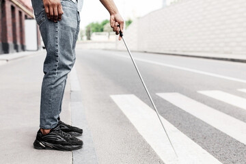 Cropped view of young black guy with vision disability standing on roadside, using walking cane in...
