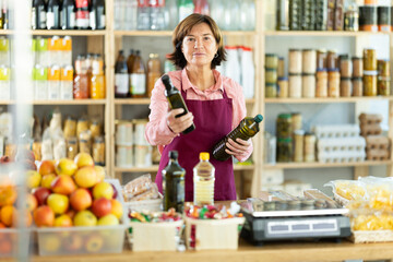 Polite mature female seller kindly offering bottled olive oil in grocery store