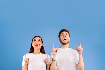Look Here. Excited couple pointing two index fingers up at copyspace isolated over pastel purple studio wall