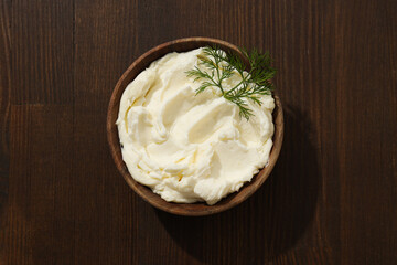 Philadelphia cheese in a wooden plate on a brown background.