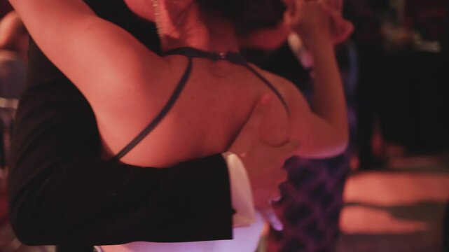 Couples dancing traditional latin argentinian dance milonga in the ballroom, tango salsa bachata kizomba lesson in red and purple lights, evening dance school class festival, performance rehearsal
