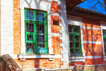 Section of old brick building with green framed windows and broken glass and metal bars. Building...