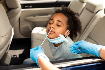 Black Preteen Girl Getting Tested For Covid-19 Sitting In Car, Traveling With Family By Automobile. Unrecognizable Medical Worker Making PCR Test For Child At Drive-Thru Diagnostic Center.