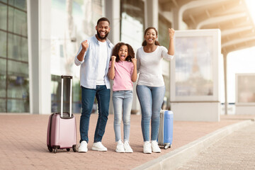 Summer Vacation Concept. Cheerful positive black family of three people having fun and shaking...