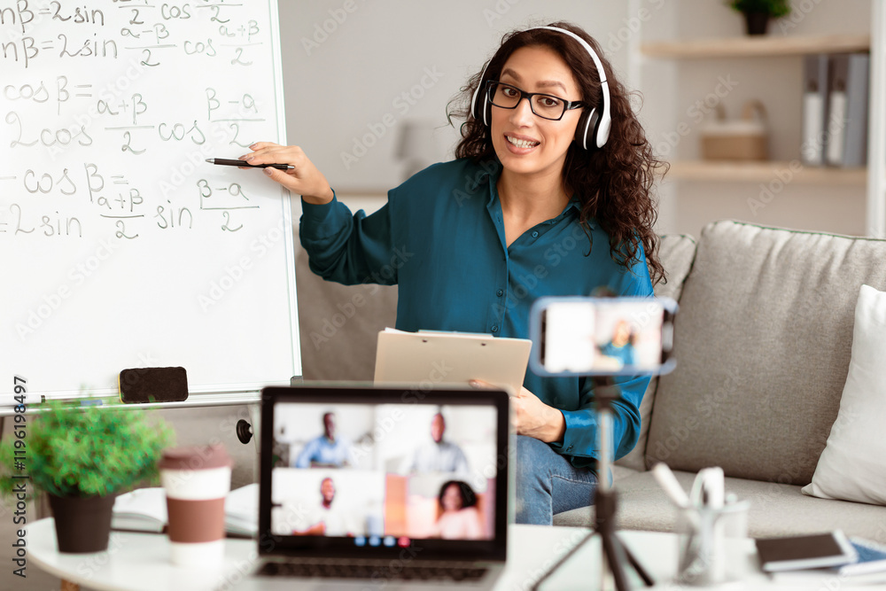 Poster Videoconference And Training. Class of diverse students learning remotely online using web app. Lady teacher in headset providing lesson looking at pc screen, recording video on cellphone on tripod
