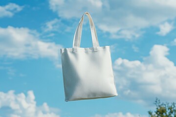 Blank white tote bag floats against a bright blue sky with fluffy clouds.
