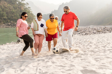 Fototapeta premium Group of senior friends playing football at sandy beach together