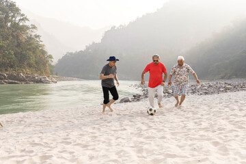Three old men having fun playing with football on beach.
