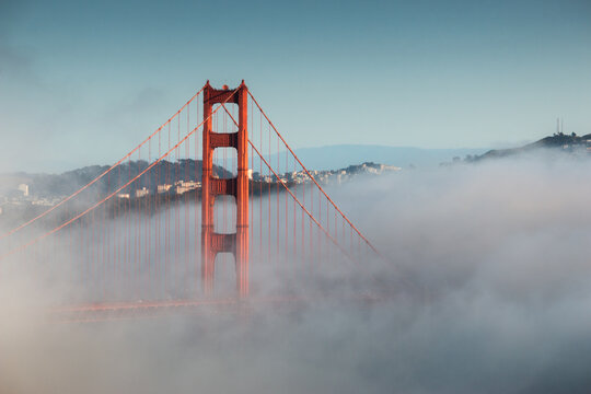 A striking view of San Francisco's Golden Gate Bridge partially cloaked in evening fog, its iconic red towers rising above the mist, symbolizing timeless beauty and engineering marvel.