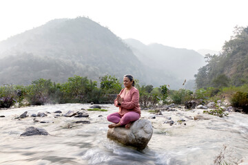 Senior woman meditating on rocks at lakeshore during vacation