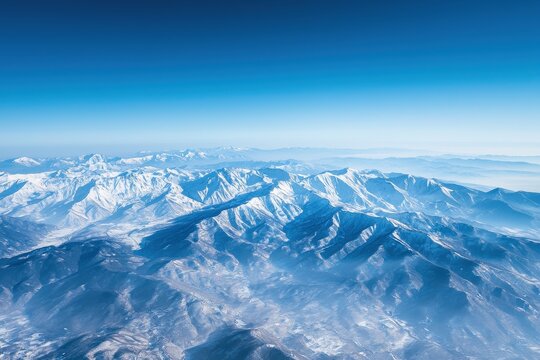 Aerial view of a mountain range covered in snow under a clear blue sky, suitable for winter travel themes