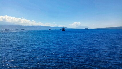 view in the middle of the blue sea during the day with a background of hills and white cloudy skies