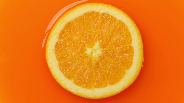 Top view of orange slice rotating on orange juice background 