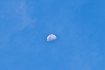 Beautiful half white moon visible on sunny daytime blue sky isolated on horizontal outdoor environment background.