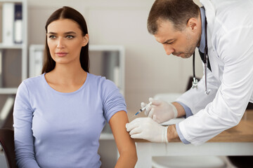 Obraz premium Immunization. Adult male doctor giving intramuscular injection to a woman. Physician injecting vaccine to patient at hospital or clinic office. Medicine cure and treatment concept