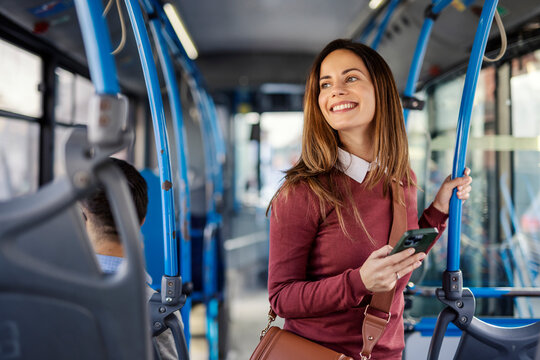 Portrait of a young woman sitting in city bus with cellphone in hands and riding public transportation.
