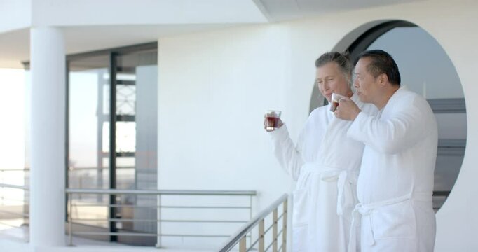 Senior couple in bathrobes enjoying coffee on balcony during vacation, copy space