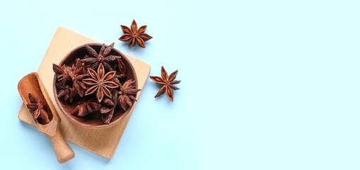 Wooden bowl and scoop with aromatic star anise on light blue background with space for text, top view