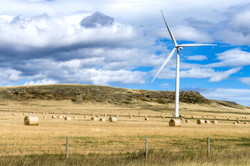 Agricultural field with bales of hay and wind power tower turbine at fall season