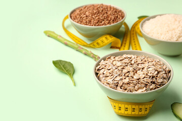 Bowls with oatmeal flakes and yellow measuring tape on green background. Diet concept