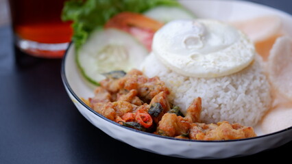 Salted egg chicken rice with sunny egg, rice crackers, slice cucumber and a glass of tea on a white plate.